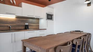 A modern kitchen with white cabinets, a wooden countertop, a built-in microwave, and a wooden dining table with chairs.