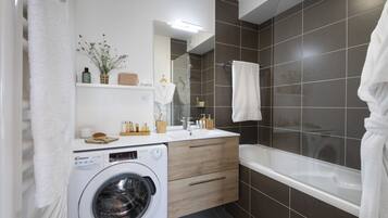 A modern bathroom with a washing machine, a sink, and a bathtub.
