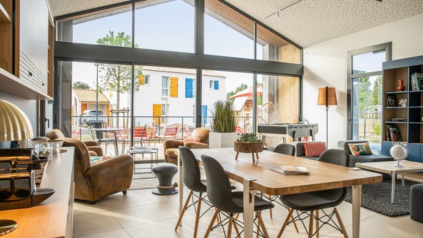 Un amplio y moderno espacio de sala de estar con una gran mesa de comedor de madera, asientos cómodos y ventanas grandes que ofrecen vistas al exterior.