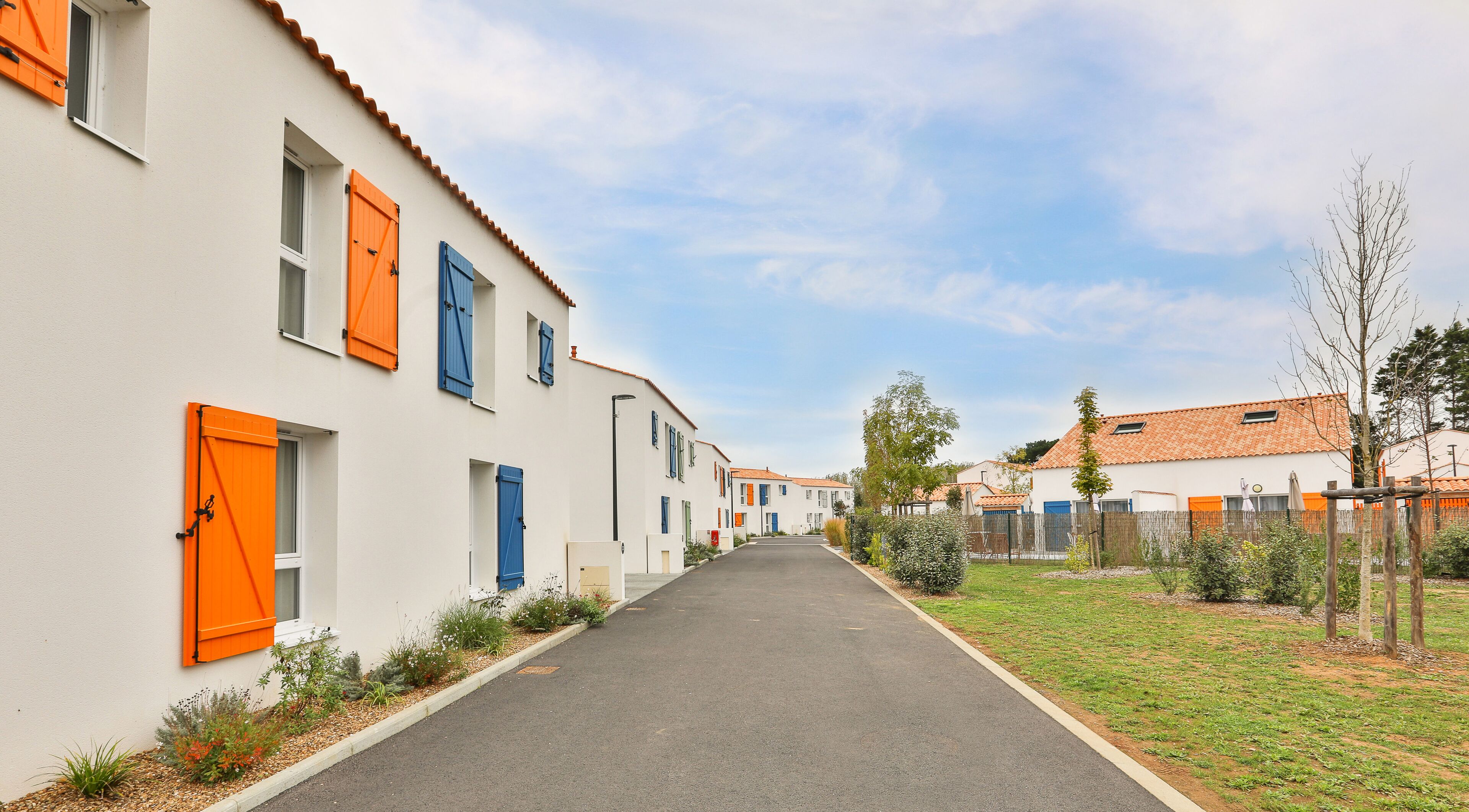 Een woonstraat met witte huizen, oranje luiken en een heldere lucht.