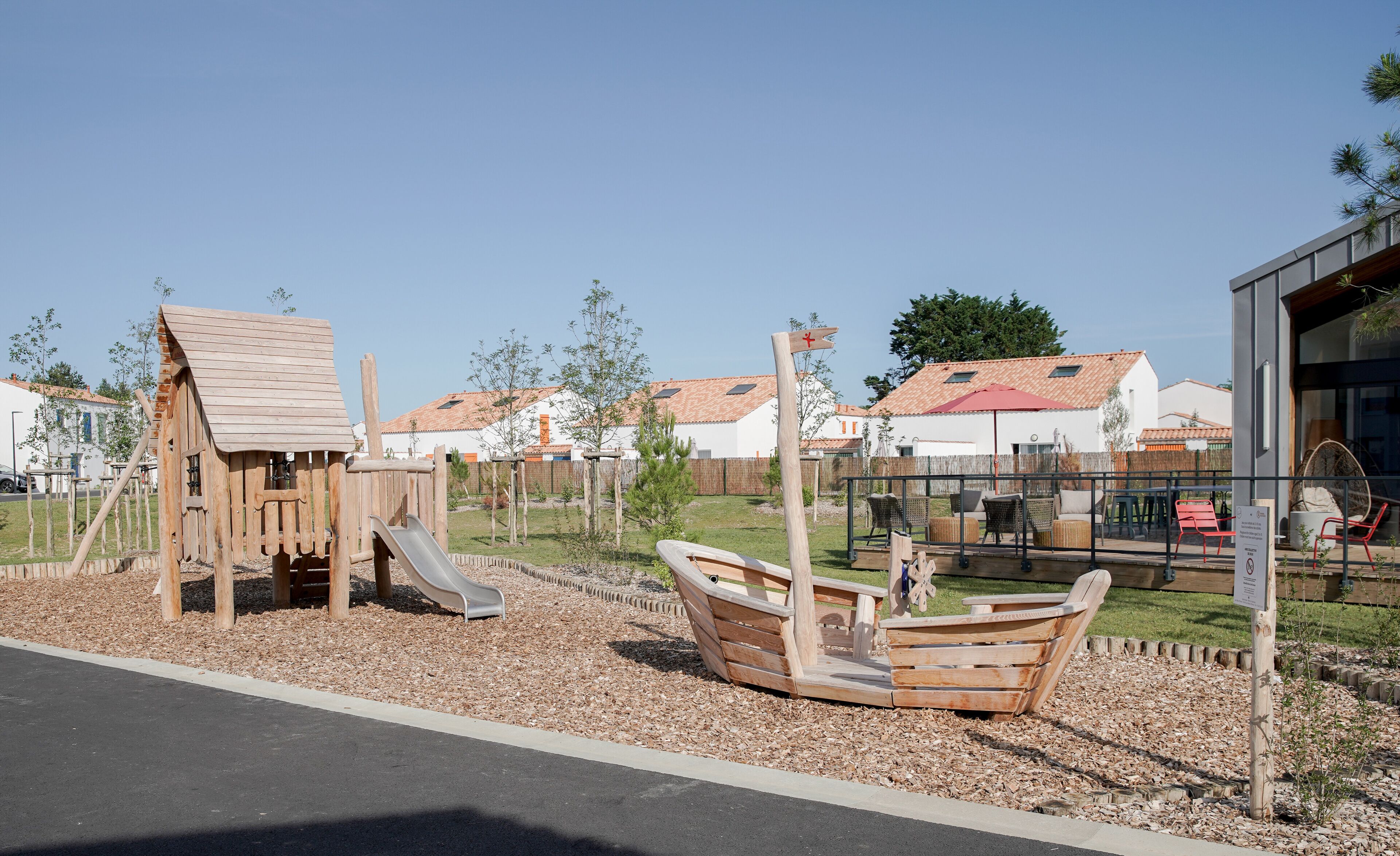 A playground with a wooden slide and swings, surrounded by a fence and mulch.