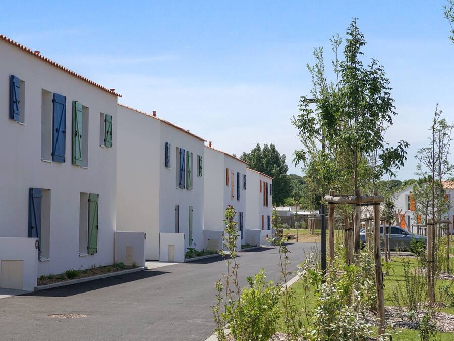 A row of white buildings with multiple windows and doors, a clear sky, and a parking area with a few cars.