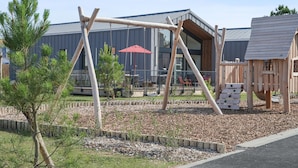Un parque infantil con columpios y una sombrilla roja, rodeado de un área ajardinada con acolchado y plantas pequeñas.