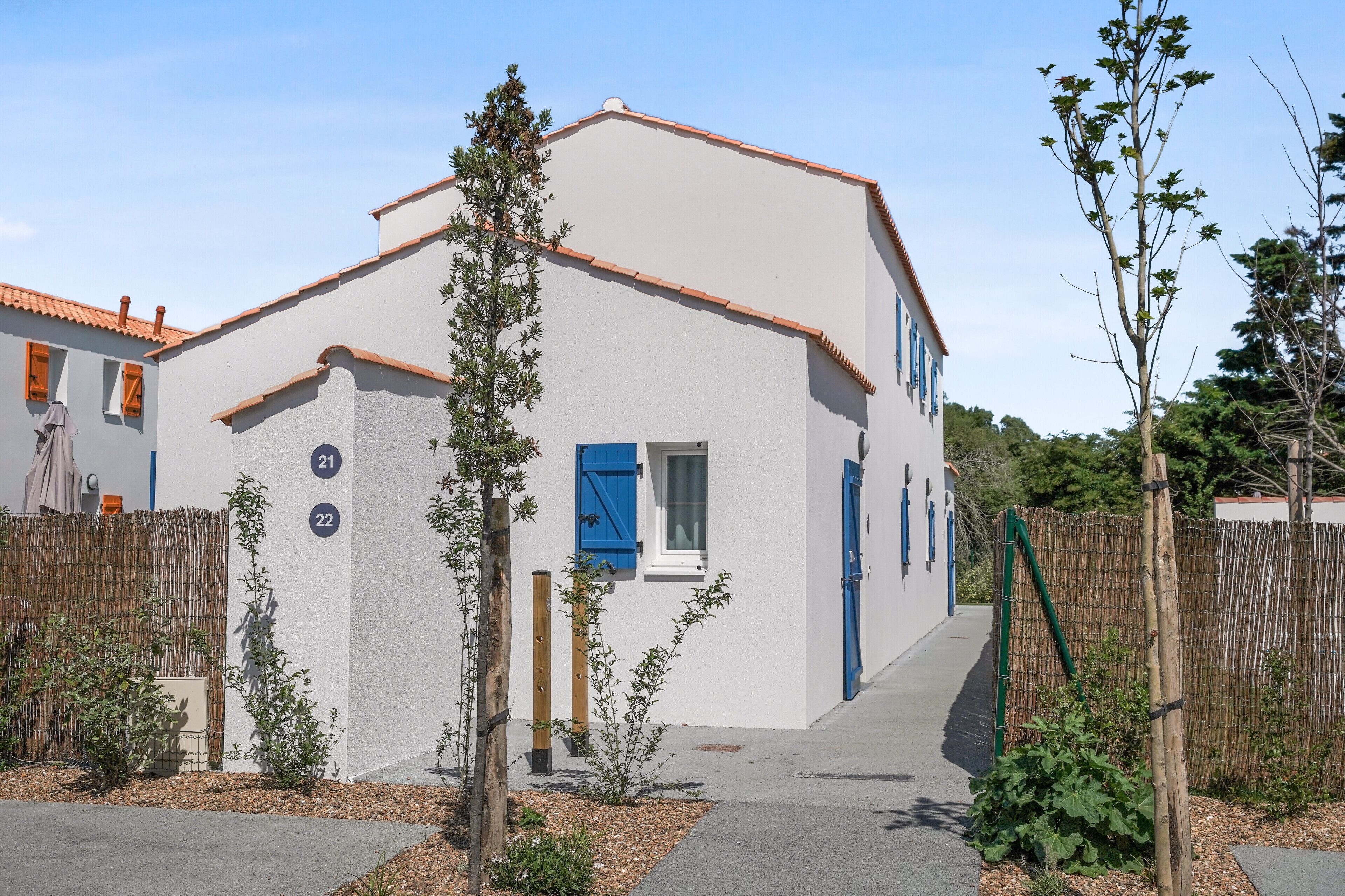 A white building with blue shutters, numbered 21 and 22, surrounded by a bamboo fence and small plants.