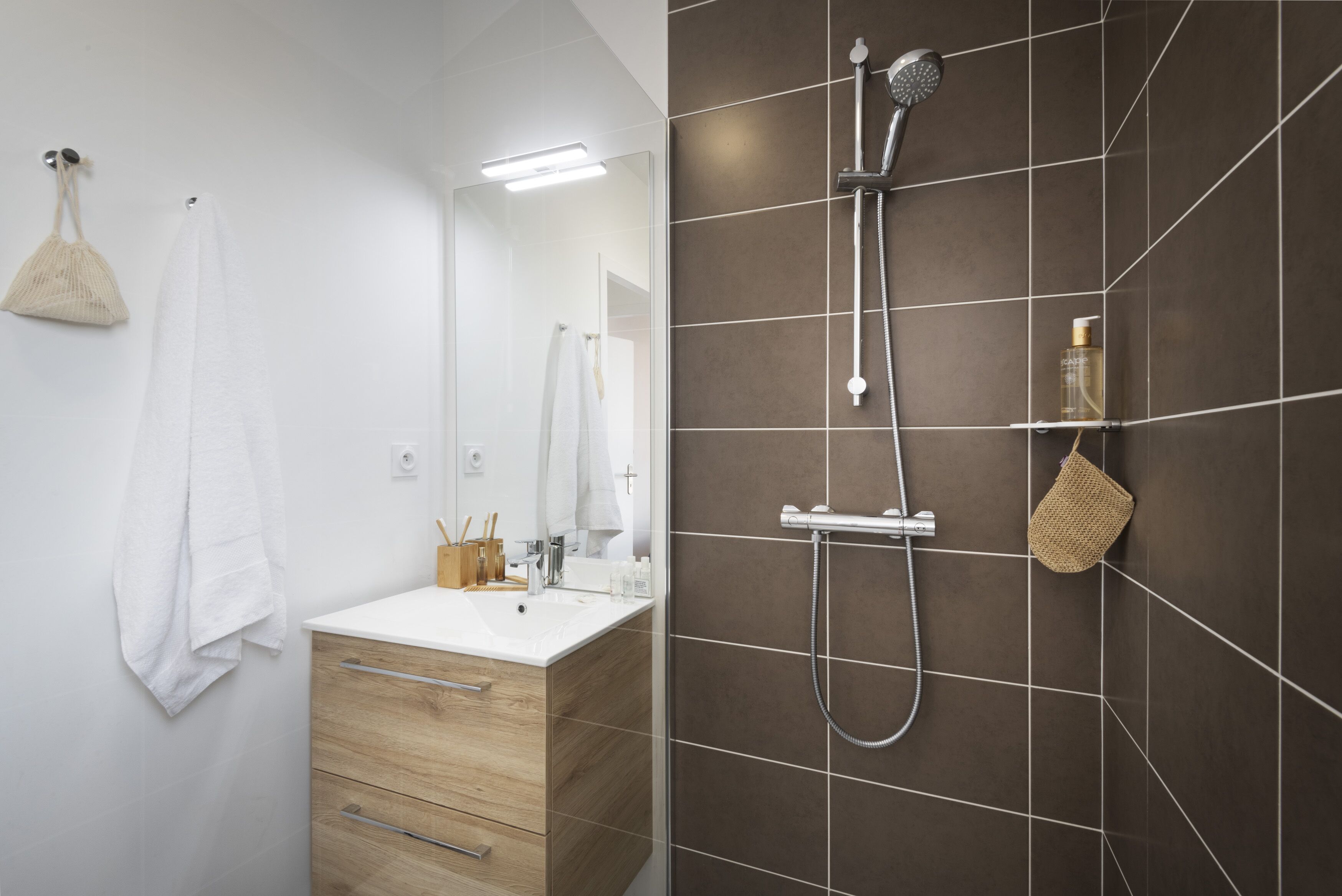 Un baño moderno con un tocador blanco, un espejo, una ducha con cabezal de ducha manual y un perchero para toallas.