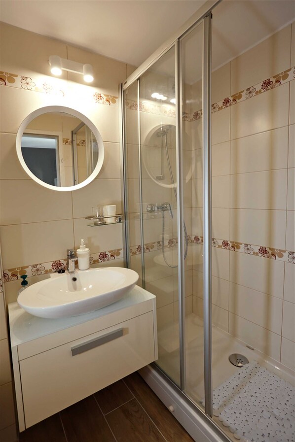A bathroom with a glass-enclosed shower, a round mirror, and a white sink with a soap dispenser.