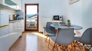 Una cucina moderna con mobili bianchi, un forno a microonde e un'area pranzo con sedie grigie e un tavolino.