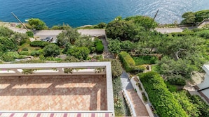 Zona residenziale con vista mare, caratterizzata da una strada asfaltata, prati verdi e un’area patio piastrellata.