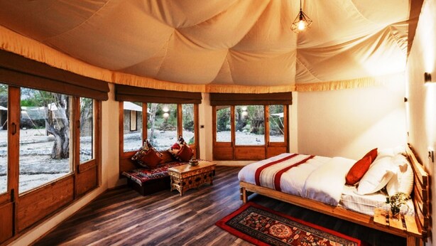 A tent-style room with a bed, seating area, and large windows.