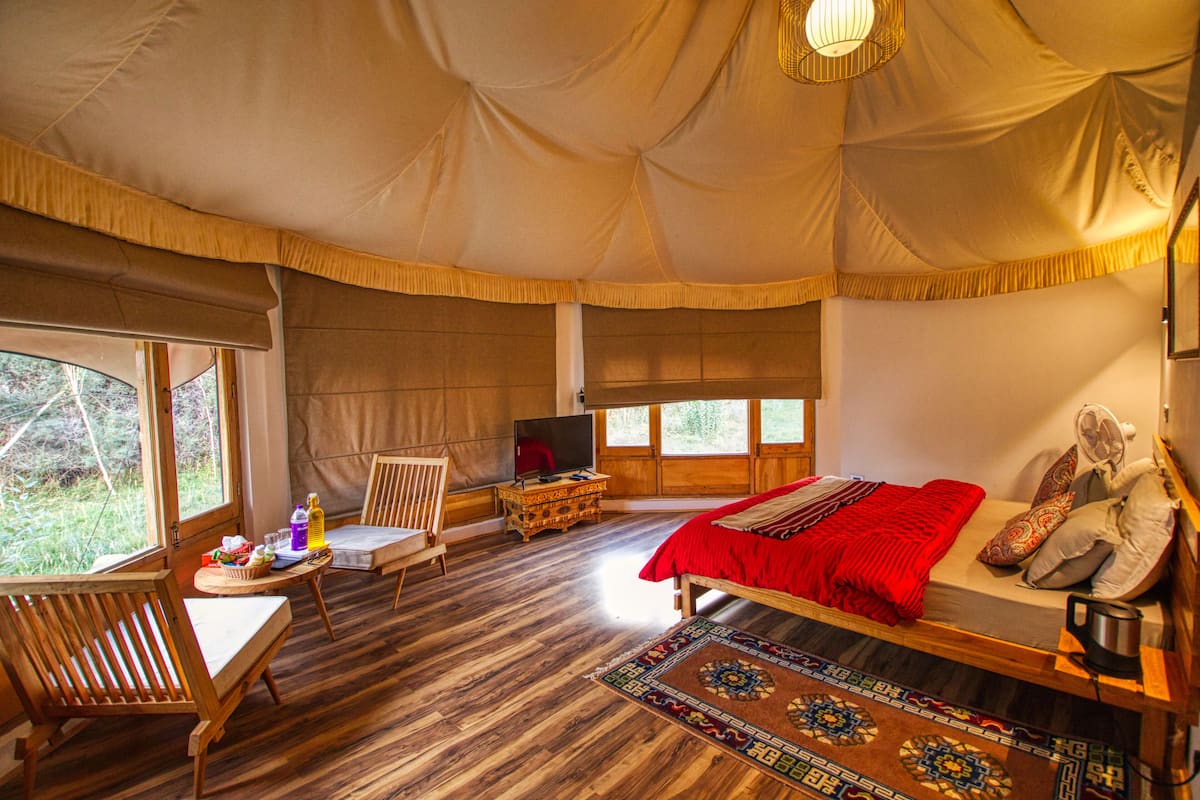 Una habitación con carpa, una cama, un televisor, una mesa de madera y una ventana.