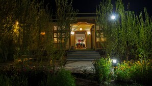 A building with a well-lit entrance, surrounded by greenery and a stone pathway leading to the door. - Chalet Seabuckthorn (Leh)