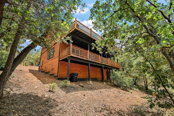 A two-story log cabin with a balcony, surrounded by trees.