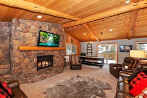 A cozy living room with a stone fireplace, a flat-screen TV, leather sofas, and a large rug.