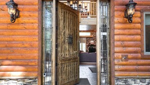 Entrada de una cabaña de madera con puerta de vidrio grande, paredes de piedra y dos faroles colgantes.