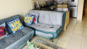 A living room with a grey sofa, a kitchen area with a refrigerator, and a tiled floor. - Innoprop @Midrand (Midrand)