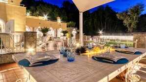 Un espace de restauration en plein air avec une table dressée pour quatre personnes, entouré de murs en pierre et de plantes en pot.