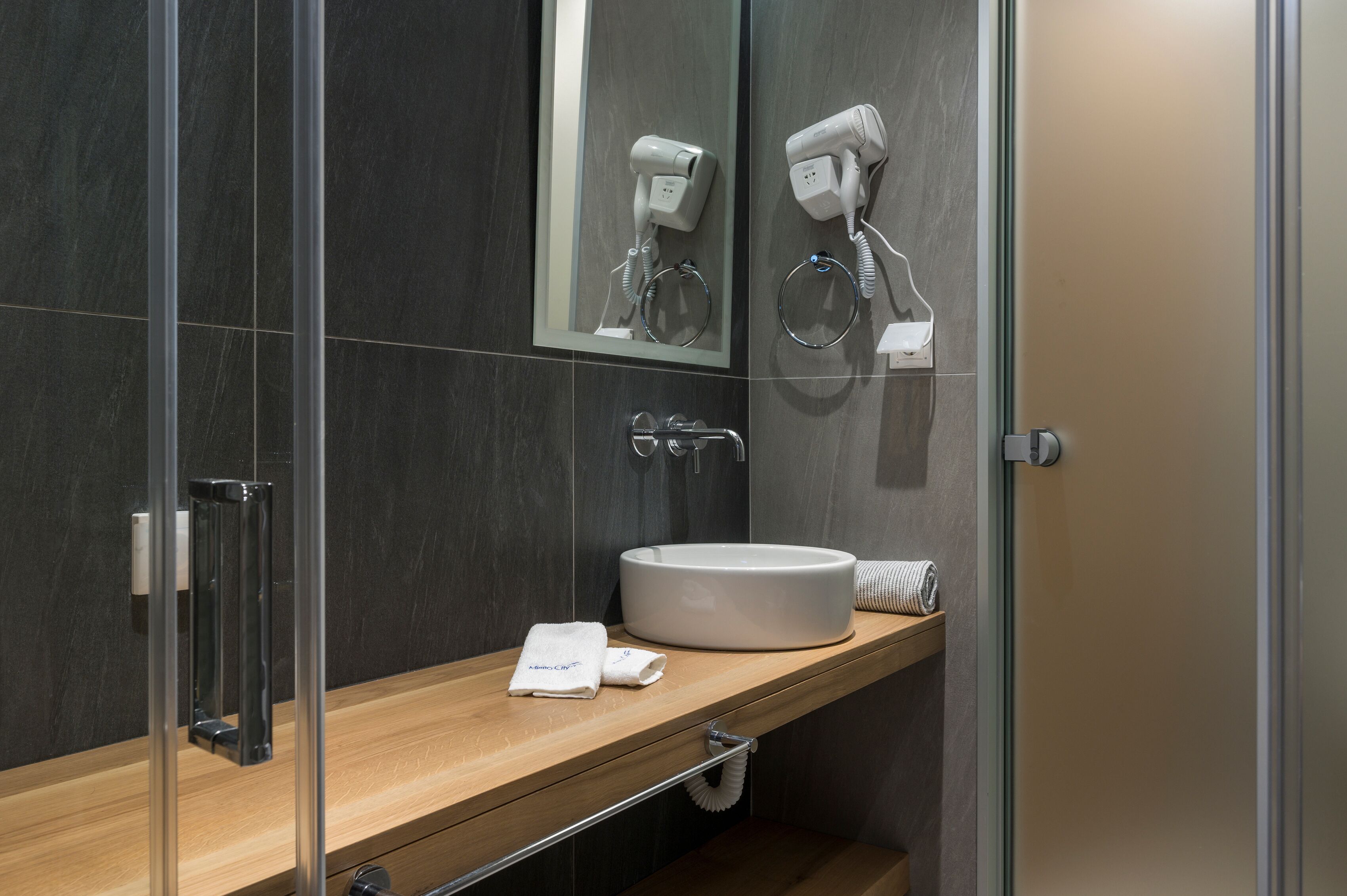 A modern bathroom with a glass shower enclosure, a wooden vanity, a white sink, and a mirror above the vanity.
