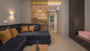 A modern living room with a sectional sofa, a wooden divider, and a kitchenette in the background. -  MIRMA CITY studio & apartment (Chania)