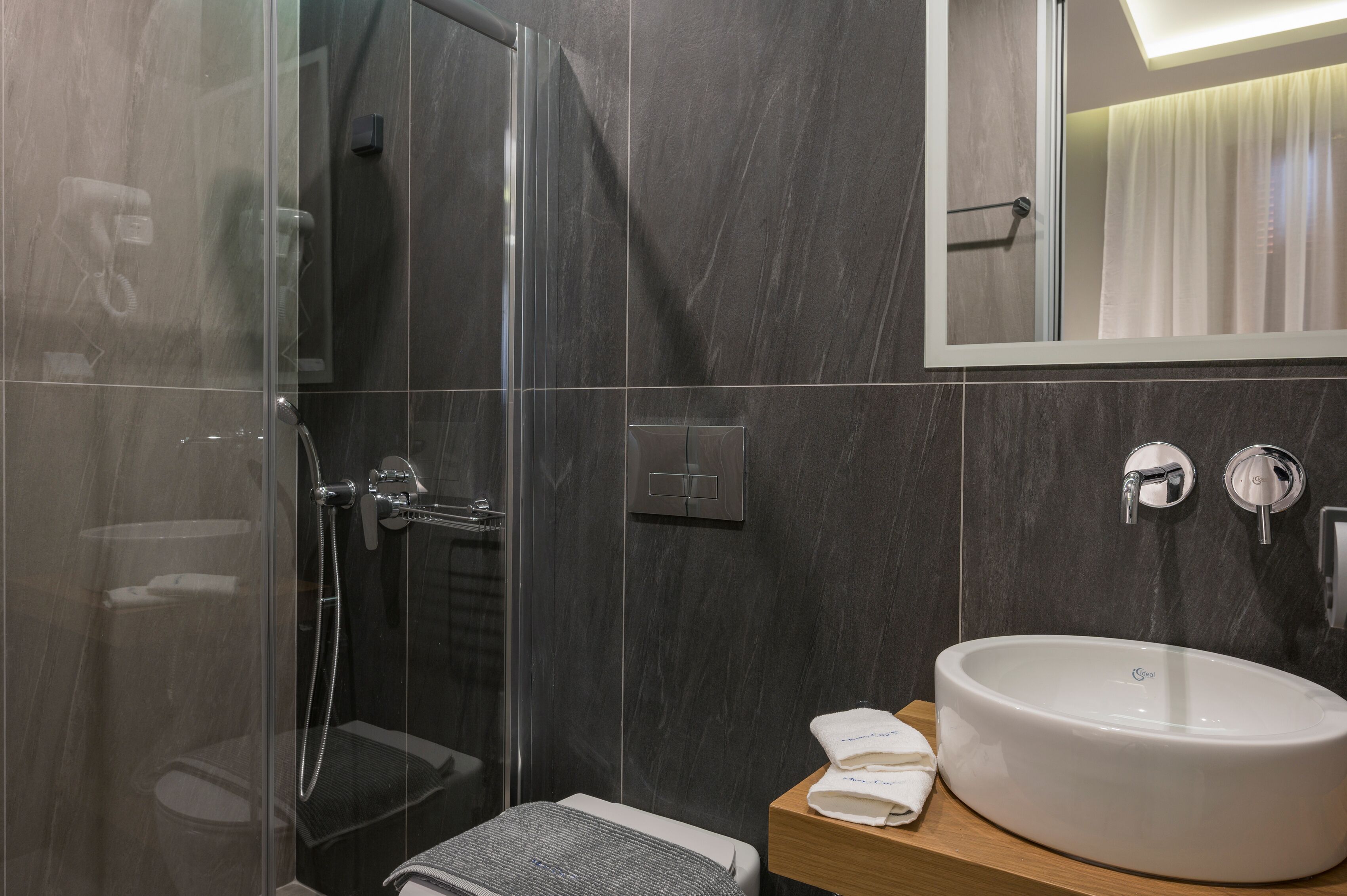 Ein modernes Badezimmer mit einer gläsernen Dusche, einem großen weißen Waschbecken und einem Spiegel darüber.