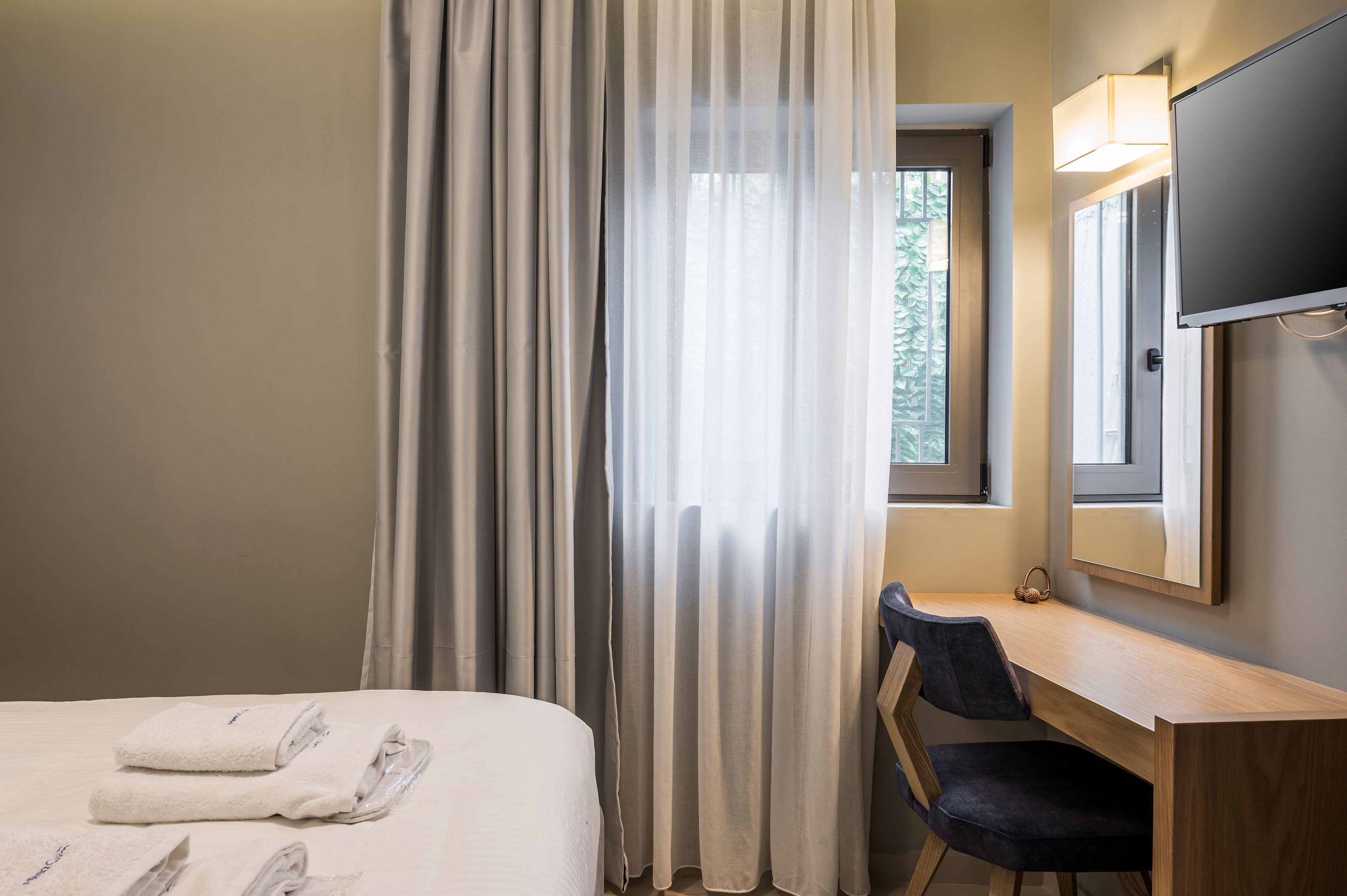 Una habitación de hotel con cama, escritorio, silla, televisor y ventana con cortinas.