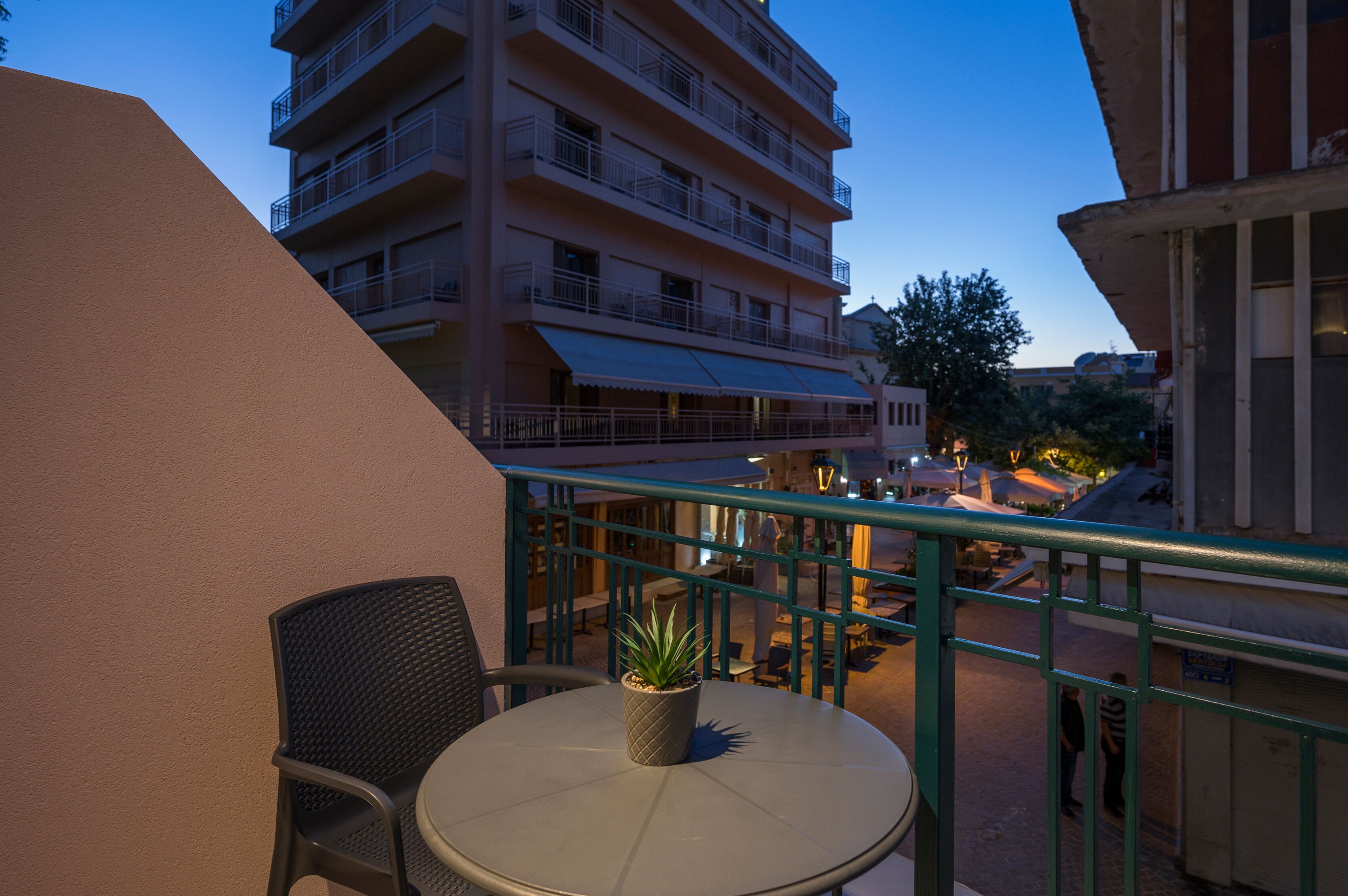 Un balcón con una mesa redonda y una silla, una planta en maceta y vistas de un edificio de varios pisos con balcones.