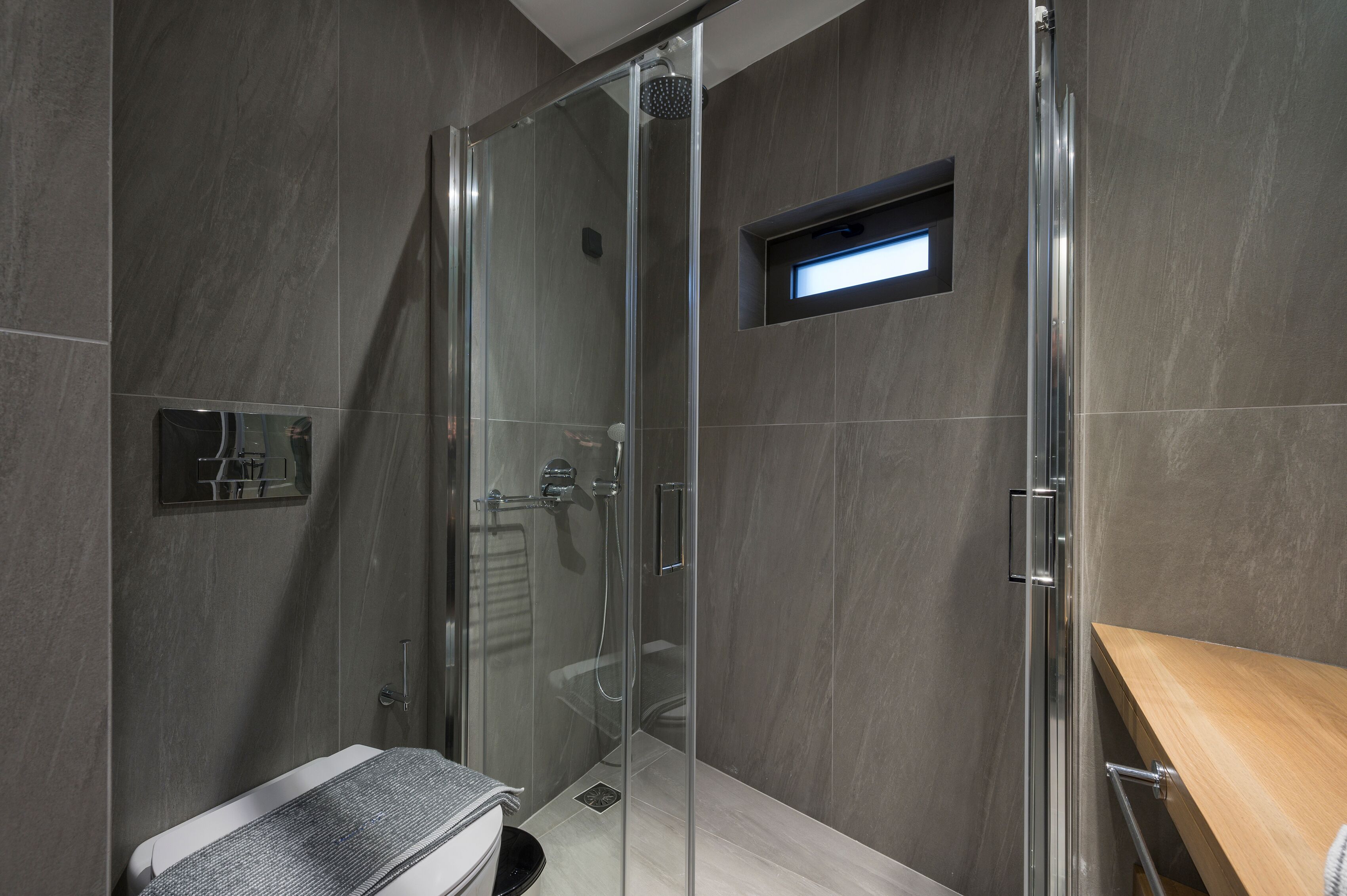 Un baño moderno con ducha envuelta en vidrio, tocador de madera y un pequeño estante con espejo.