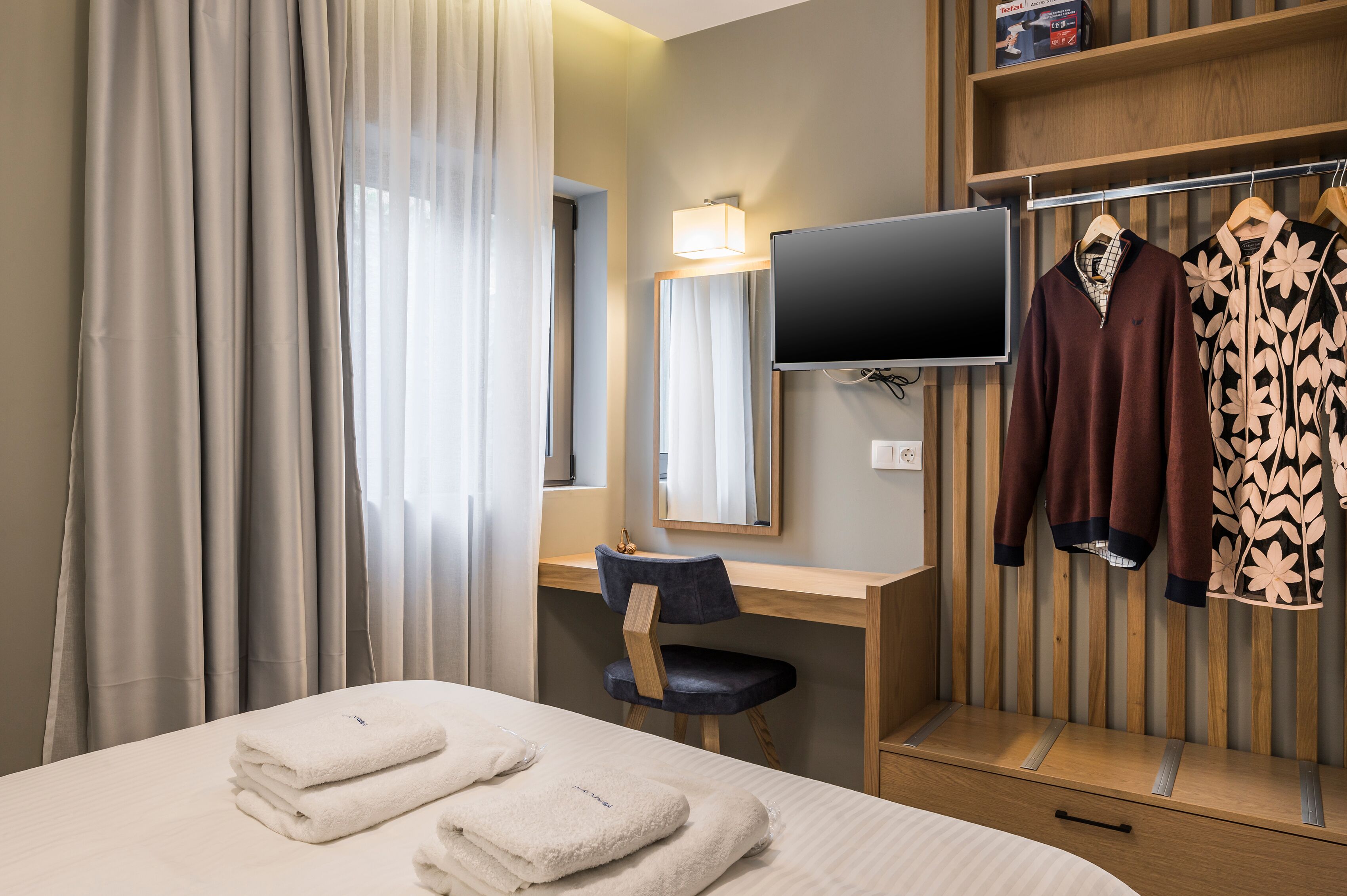 A hotel room with a bed, a desk, a chair, a TV, and a wardrobe.