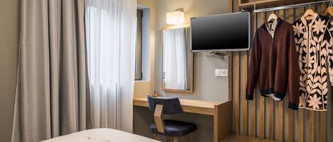A hotel room with a bed, a desk, a chair, a TV, and a wardrobe.