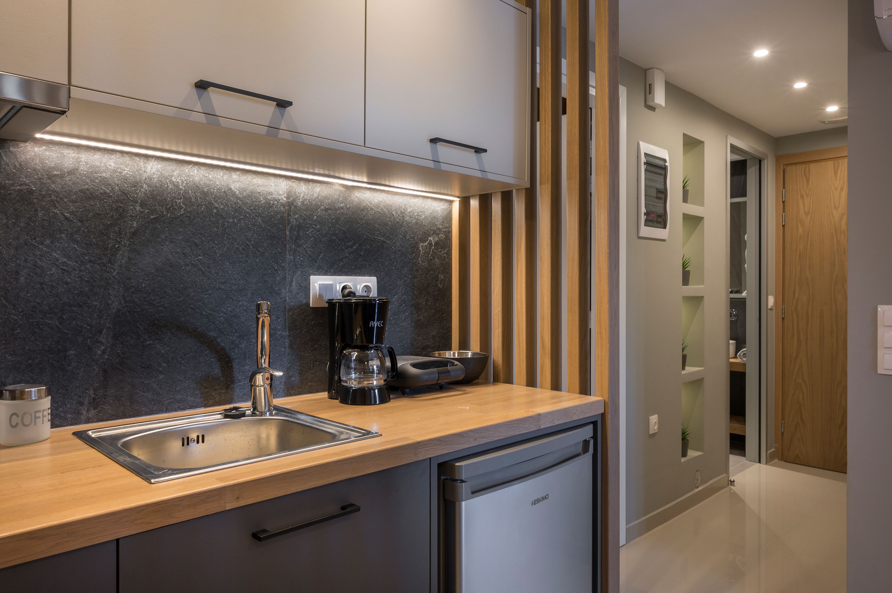 Una cocina moderna con un lavamanos de acero inoxidable, una cafetera y un tostador. Hay una encimera de madera y un armario sobre el lavamanos.