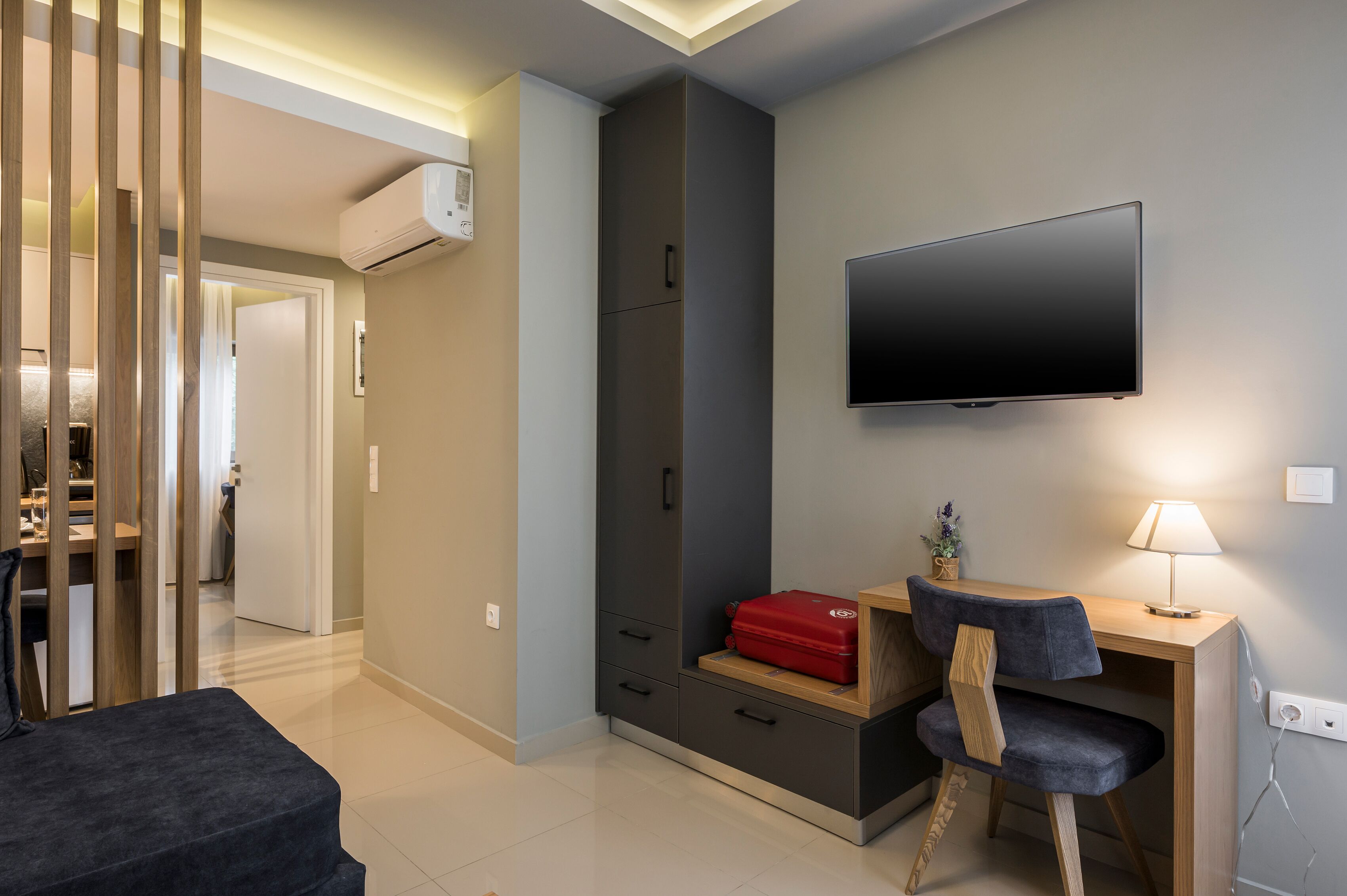 Ein modernes Wohnzimmer mit Fernseher, Schreibtisch mit Lampe und einem roten Koffer auf dem Schreibtisch.
