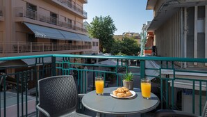 A balcony with a table set for breakfast, including croissants and orange juice, overlooking a cityscape with buildings and a tree. -  MIRMA CITY studio & apartment (Chania)