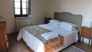 Ein Schlafzimmer mit Bett, Fenster, Heizkörper, Nachttisch und einem Holzschrank.