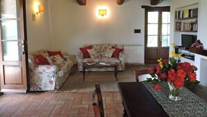 Ein gemütliches Wohnzimmer mit Holzboden, einer Sofagarnitur, einem Couchtisch und einem Esstisch mit Blumen.