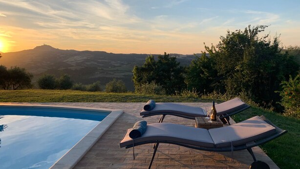 Ein Poolbereich mit Liegestühlen und einer Weinflasche, mit Blick auf eine schöne Landschaft aus Hügeln und Bäumen.