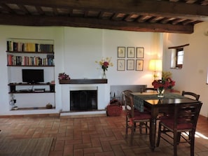 Un salon avec une cheminée, un téléviseur, une bibliothèque et une table à manger avec des chaises.