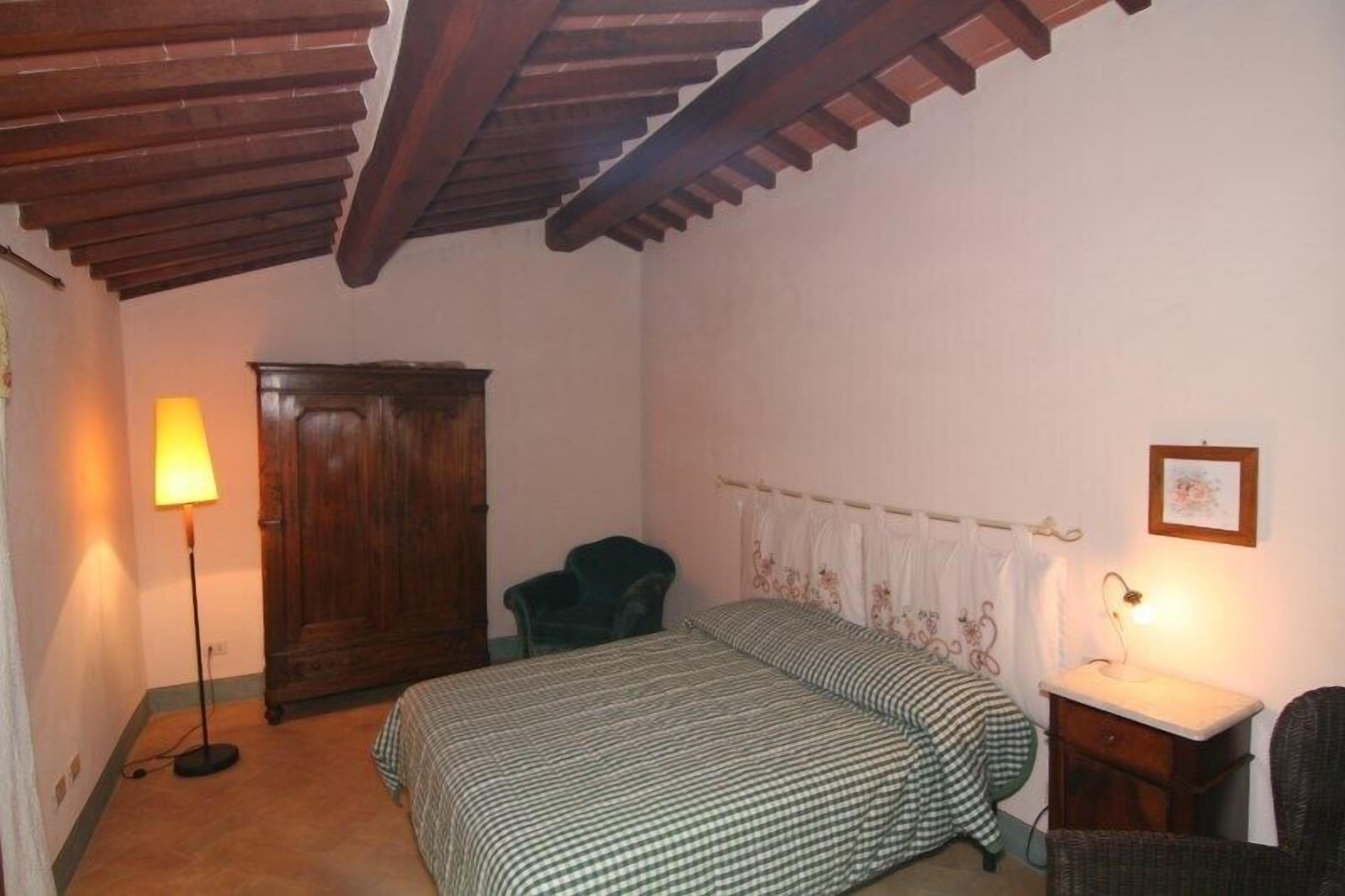 Une chambre avec un plafond en bois, un lit avec une literie à carreaux, une table de chevet, une chaise, une armoire et une lampe.