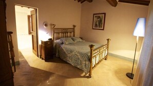 A bedroom with a wooden bed, a nightstand, a lamp, and a painting on the wall. - PODERE OLIVETO Radicofani (SI) (Radicofani)