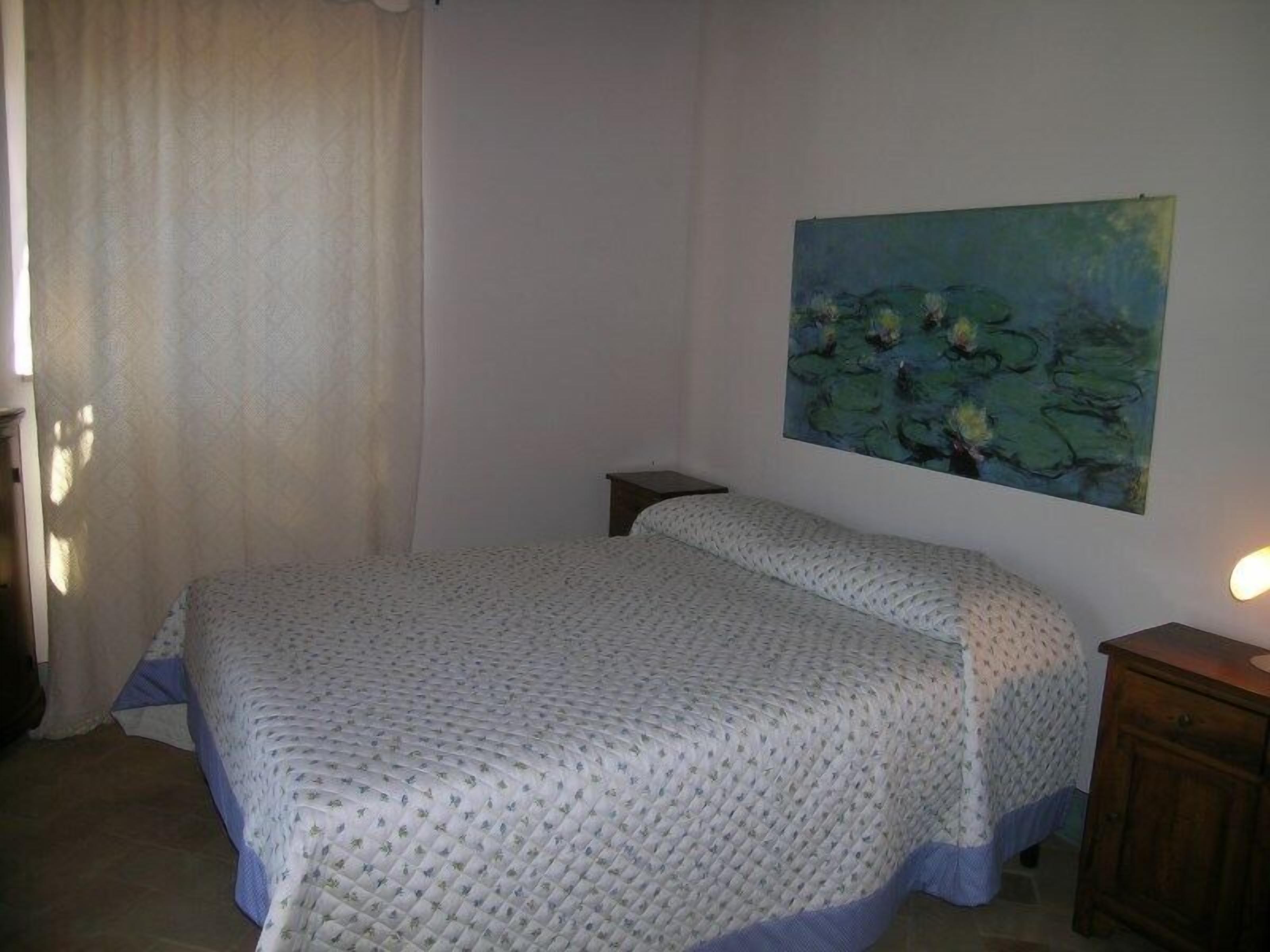 Una camera da letto con un letto, un comodino, un quadro e un armadietto in legno.