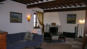 A cozy living room with a blue sofa, a fireplace, and two paintings on the walls. - PODERE OLIVETO Radicofani (SI) (Radicofani)