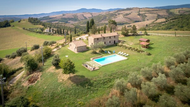 A stone villa with a swimming pool and sun loungers, surrounded by lush greenery and rolling hills. - PODERE OLIVETO Radicofani (SI) (Radicofani)