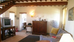 A cozy living room with a wooden staircase, a television on a stand, a cabinet, a sofa, and a lamp. - PODERE OLIVETO Radicofani (SI) (Radicofani)