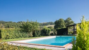 A rectangular swimming pool with a clear blue water surface, surrounded by a well-maintained lawn and a wooden pergola structure.
