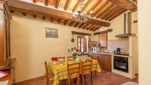 A dining area with a table set for four, wooden chairs, a chandelier, and a kitchen in the background.