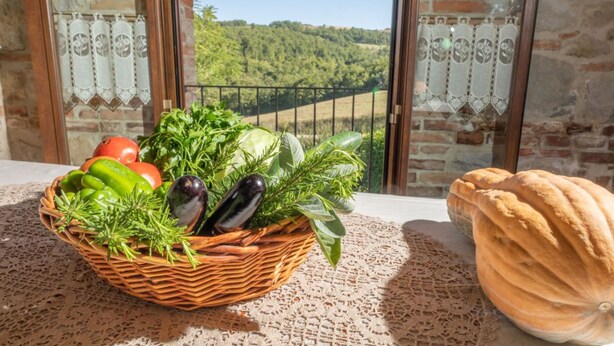 A wicker basket filled with vegetables and a loaf of bread on a balcony with a scenic view.