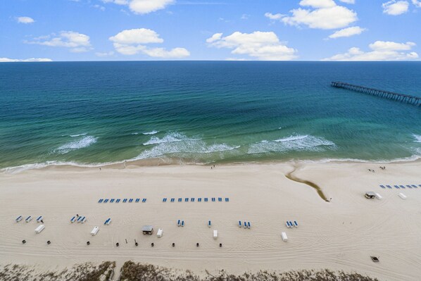 A beach with rows of sun loungers and a pier extending into the ocean. - Calypso 2003W | 20th-Floor Gulf Views, Beach Service Included, Steps from Pier Park (Panama City Beach)