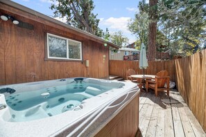 Une terrasse en bois avec un jacuzzi, une table et des chaises.