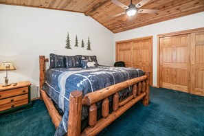 Une chambre avec un lit en bois, un ventilateur de plafond et une grande armoire.