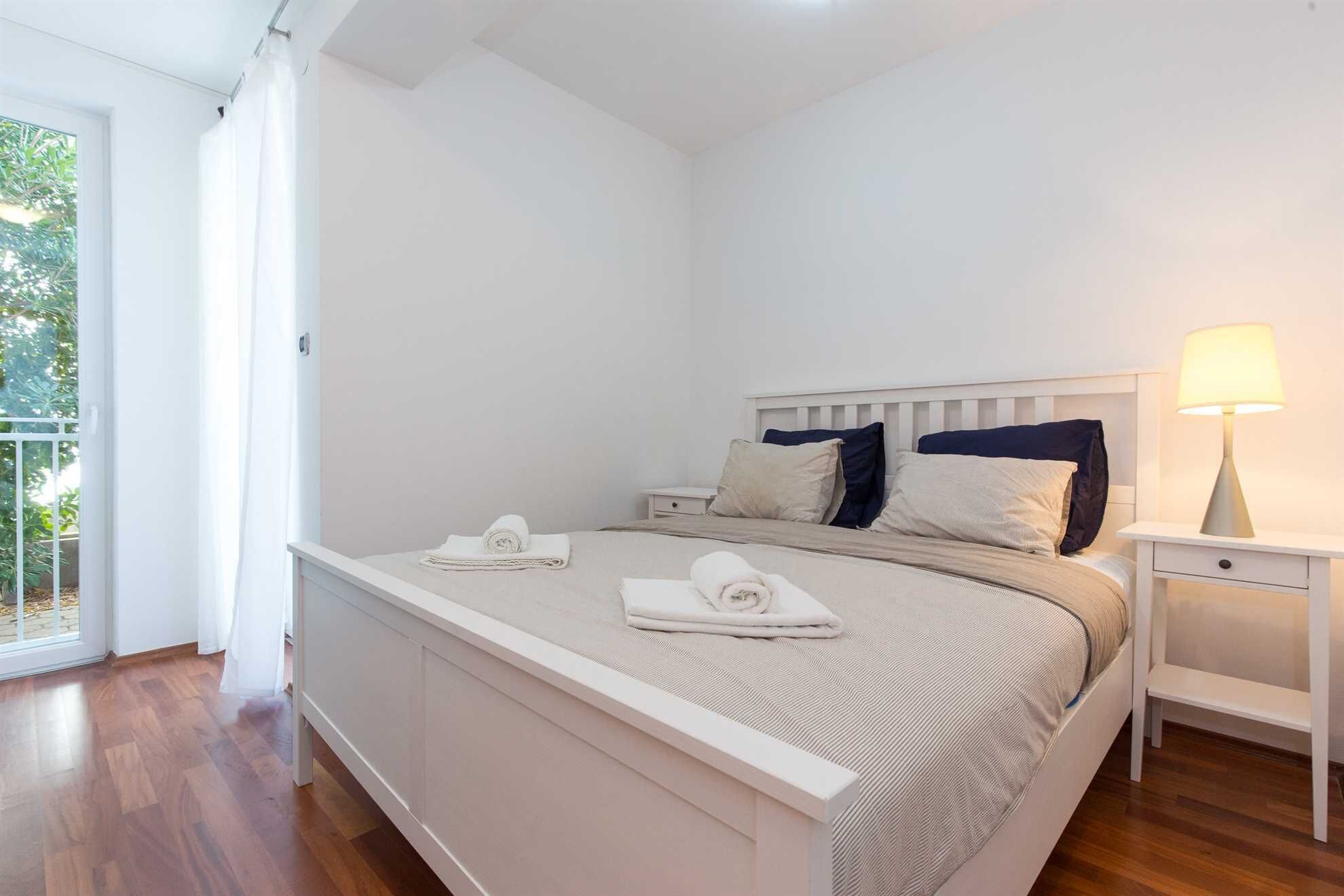 Une chambre à coucher avec un lit, deux tables de chevet, une lampe et une vue sur la verdure.