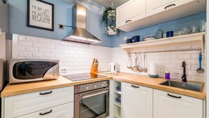 Een moderne keuken met witte kastjes, een roestvrijstalen fornuis, een magnetron en een hangplant.