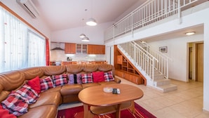 A spacious living area with a leather sofa, a wooden dining table, and a staircase leading to an upper floor. - Extraordinary Villa Damir (Baška)